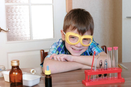 家庭化学实验。穿着格子衬衫的微笑男孩坐在桌旁, 去做化学实验
