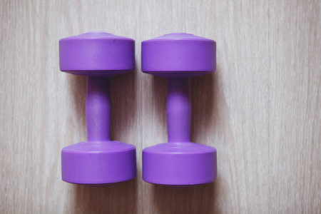 木制背景上的两个紫色塑料哑铃。健身，健美，健康的生活方式..