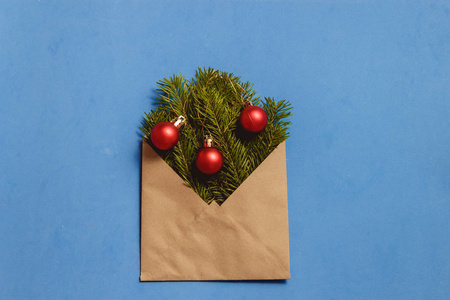 顶部视图绿色冷杉树枝和红色装饰在棕色工艺信封在蓝色背景