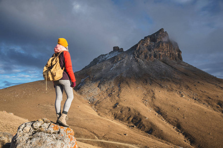 一位女旅行者的背部肖像, 穿着一件带着帽子的夹克, 背包站在一个有