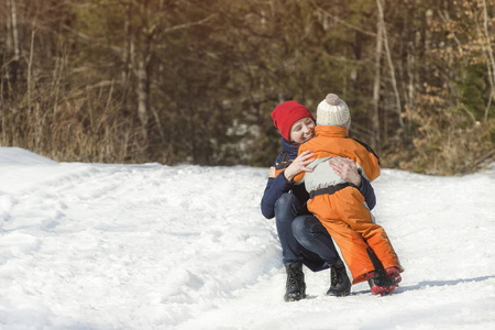 妈妈在松林的背景上拥抱了这个小儿子。 针叶林冬季雪日