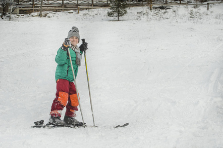 滑雪板上的男孩带着滑雪杆微笑。 冬天。