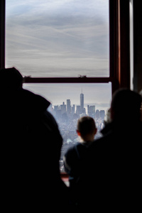 一个孩子透过帝国大厦的窗户，观察甲板与曼哈顿下城和一个世界贸易中心的背景。
