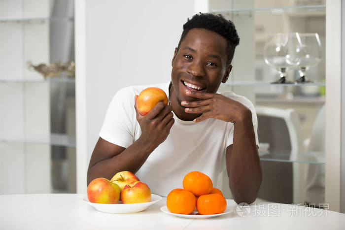 英俊微笑的非洲男人把苹果放在白色厨房的肖像，健康的概念