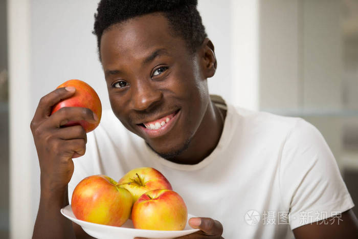 英俊微笑的非洲男人把苹果放在白色厨房的肖像健康的概念