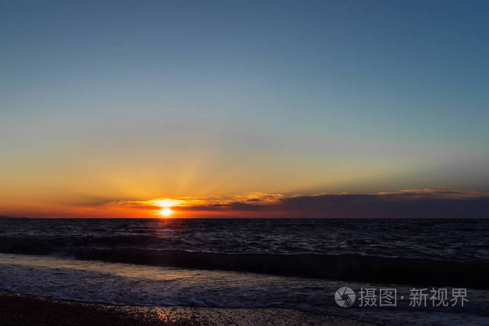 太阳在云层中发散的光线. 小小的海浪. 美丽的傍晚风景.