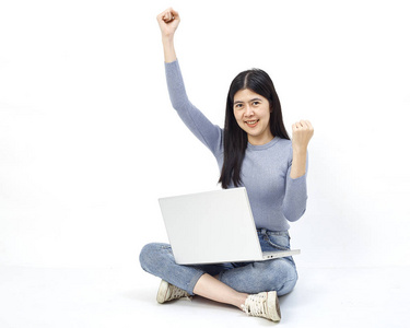 商业概念。 一个微笑的休闲女孩的肖像，她拿着笔记本电脑，坐在地板上，在白色背景上做着快乐的手势。