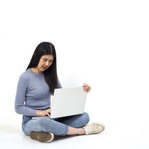 商业概念。 一个微笑的休闲女孩的肖像，她拿着笔记本电脑，坐在地板上，在白色背景上做着快乐的手势。
