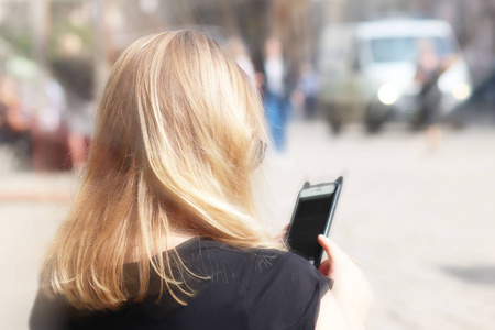 年轻漂亮的金发女孩在旧城街道的智能手机上交流。 日常交流中的小工具。 现代社会交流中的新技术。 历史上的学生。图片