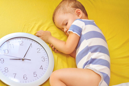 可爱的两岁小男孩睡在床上，带着一个大钟