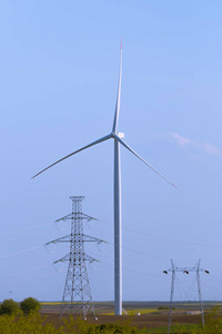 风力涡轮机在农业领域与大电塔在前面，蓝天在背景。