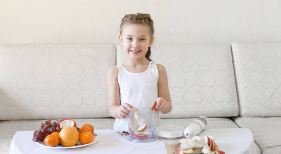 孩子把水果片放进搅拌机里。女孩把切好的苹果和梨放在搅拌机里做果汁和鸡尾酒。