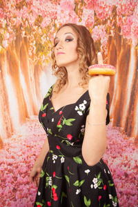 美丽的年轻女孩站在黑色别针装扮和玩釉粉红色甜甜圈乐趣