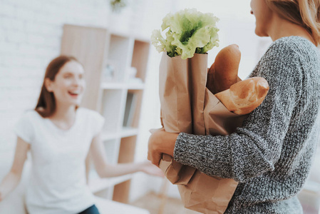 妈妈带着家里商店里的一包食物。 女儿在帮妈妈。 健康的食物和生活方式概念。 一起做饭。 包里有面包。 母女在家。 少女。