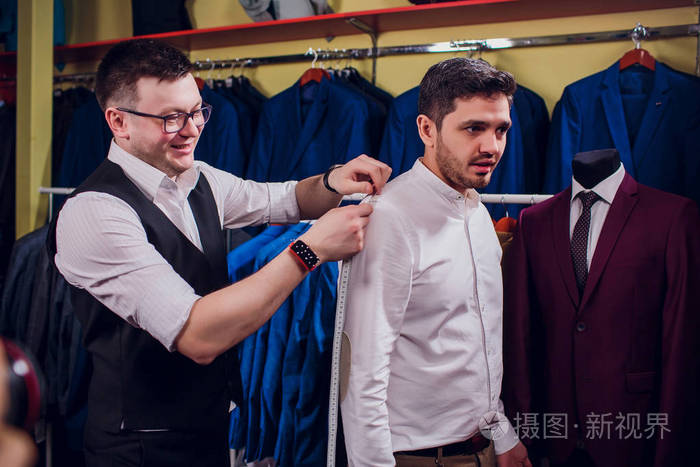 商人在商店里穿经典背心对排服.男人在服装店里帮另一个试穿西装