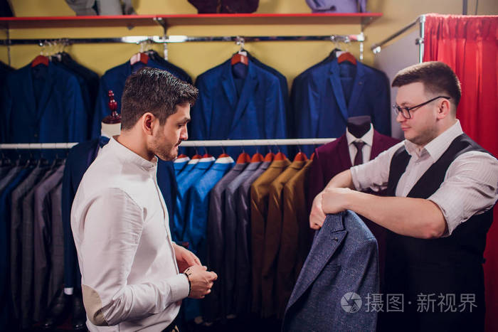 商人在商店里穿经典背心对排服男人在服装店里帮另一个试穿西装