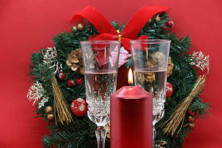 两杯香槟，一支燃烧的红烛，一个红色背景上的花环。