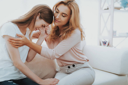 女人在家安慰不幸的十几岁的女儿。 坐在家里的沙发上。 有问题的女孩。 家庭冲突。 父母和孩子。 不开心的女孩。 交流概念。 关系