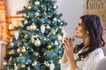 圣诞快乐的年轻女子穿着白色针织衫，在家喝咖啡或茶