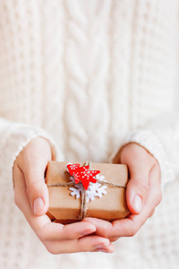 穿针织毛衣的女人拿着圣诞礼物，用手工纸包装，上面有毛毡雪花和红杉树。 新年DIY礼物。