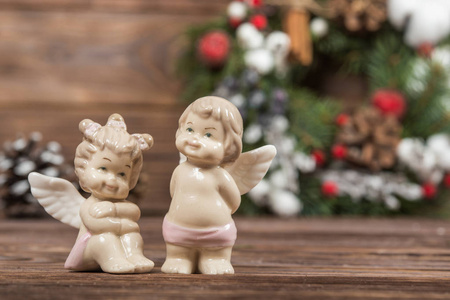 两个小天使形象，一个女孩和一个男孩。 圣诞装饰品。 花环。 圣诞节冬季框架在黑暗的木制背景。 红色元素