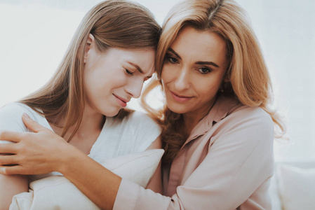 女人在家安慰不幸的十几岁的女儿。 坐在家里的沙发上。 有问题的女孩。 家庭冲突。 父母和孩子。 不开心的女孩。 交流概念。 关系