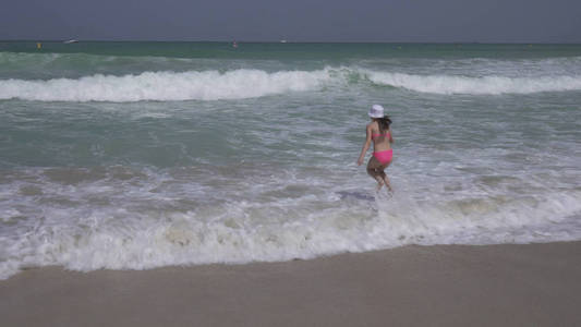 身穿游泳衣的少女在迪拜海滩上的波斯湾海浪中愉快地跳来跳去