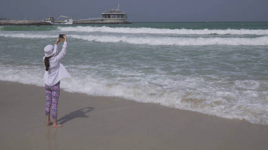 在波斯湾 迪拜 海岸的公共朱美拉开放海滩上, 十几岁的女孩在智能手机上拍摄海浪
