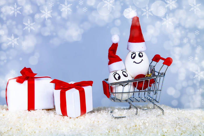 两个鸡蛋在圣诞帽上放在雪上的购物车上。 圣诞节购物。 圣诞义卖。