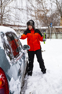 少年穿着一件橙色夹克，在冬天把车从雪中擦干净。