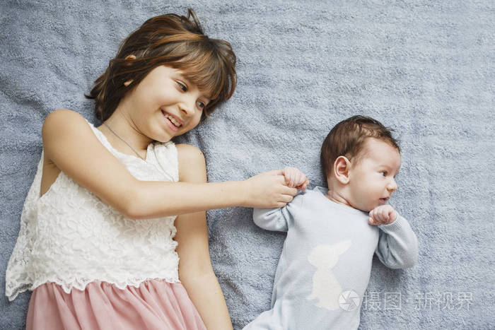 可爱的快乐女孩抱着她刚出生的小弟弟灰色背景漂亮的男婴在蓝色的衣服