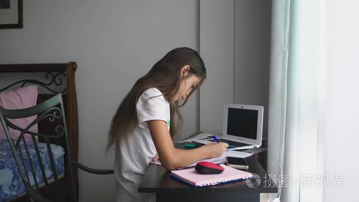 十几岁的女孩在她的房间里, 在桌子上为学校做作业