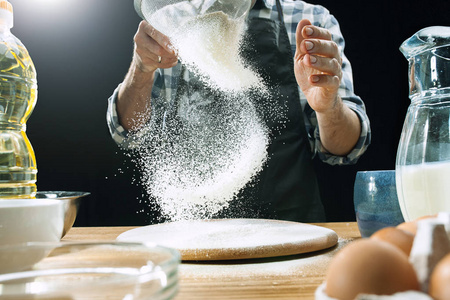专业的男性厨师在厨房的桌子上洒面团和面粉预贴或烤面包
