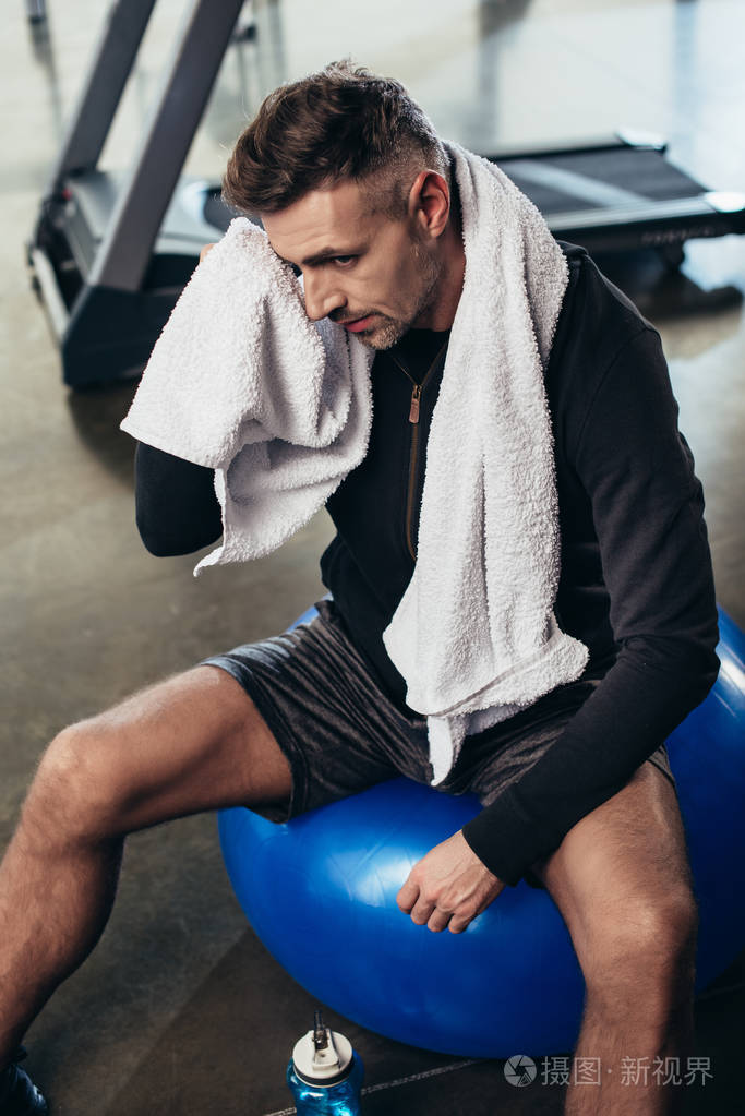 疲惫的英俊运动员用毛巾坐在健身球上的高角度视角