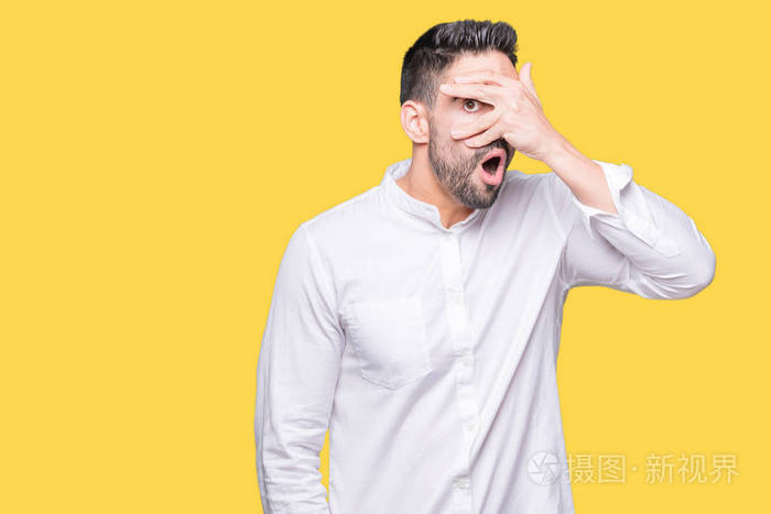 年轻的商人在孤立的背景下偷看,震惊地遮住脸和眼睛