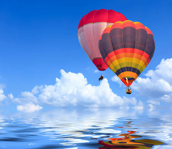 在蓝天上空飞行的彩色热气球与水的反射
