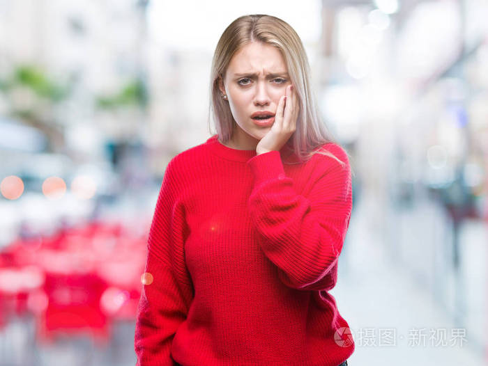 年轻的金发女人穿着冬天的毛衣，在孤立的背景上，用手触摸嘴，因为牙痛或牙齿上的牙齿疾病，表情痛苦。 牙医的概念。