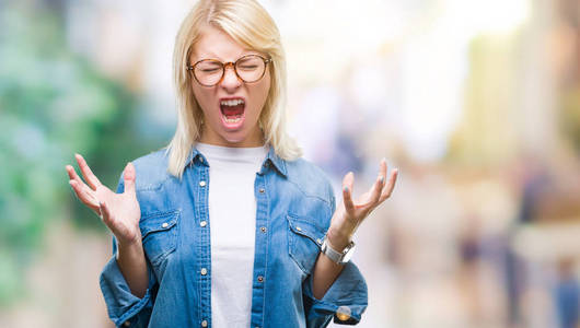 年轻漂亮的金发女人戴着眼镜，在孤立的背景上庆祝疯狂和疯狂的成功，手臂抬起和闭上的眼睛尖叫兴奋。 赢家概念