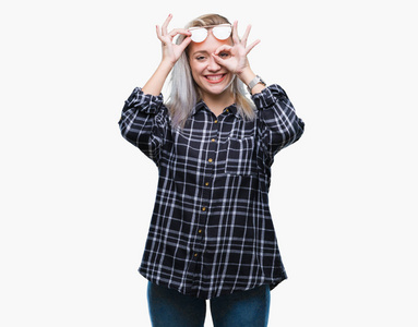 年轻的金发女人戴着太阳镜在孤立的背景上做着好的手势，用手微笑的眼睛透过手指看着幸福的脸。