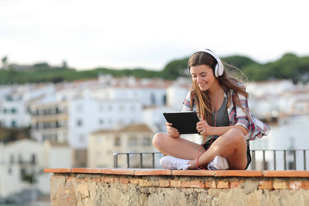 快乐的青少年戴着耳机，在平板电脑上观看和收听在线视频，坐在度假的窗台上