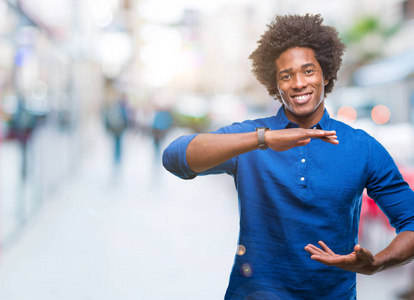 美国黑人男子在孤立的背景上用手做手势，显示大尺寸的标志，测量符号。笑着看着镜头..衡量概念。