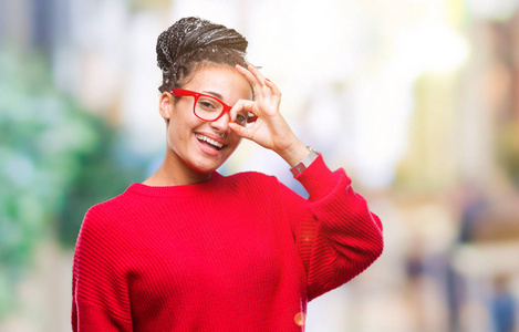 年轻的辫子非洲裔美国女孩穿着毛衣和眼镜，在孤立的背景下做着好的手势，用手微笑，用眼睛看着手指快乐的脸。