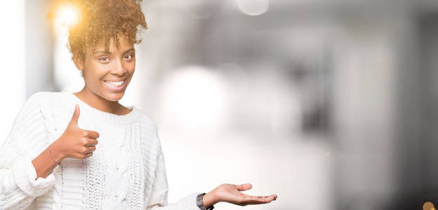 美丽的年轻的非洲裔美国妇女穿着冬季毛衣，在孤立的背景下，伸出手掌，竖起大拇指，做着好的手势，微笑，快乐和快乐