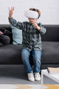 儿童坐在沙发上，在家里使用虚拟现实耳机