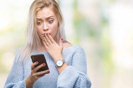 年轻的金发女人用智能手机在孤立的背景封面上发短信，手因错误而震惊，恐惧的表情，沉默中的恐惧，秘密的概念