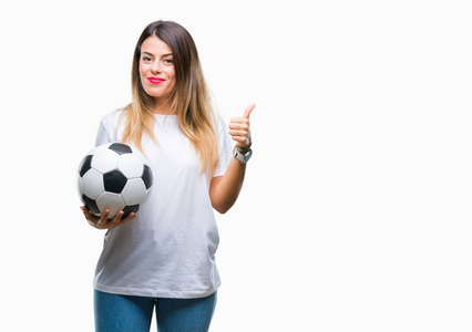 年轻漂亮的女人抱着足球在孤立的背景上快乐的大笑着做，好的，用手指签拇指，好的标志