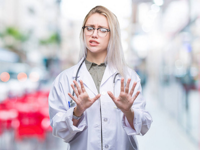 年轻的金发医生女人在孤立的背景下厌恶的表情，不高兴和恐惧的做厌恶的脸，因为厌恶的反应。 举起双手。 令人讨厌的概念。