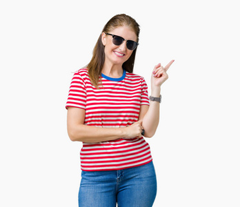 中年成熟的女人戴着太阳镜在孤立的背景上，脸上挂着一个大大的微笑，用手和手指指向一边，看着相机。