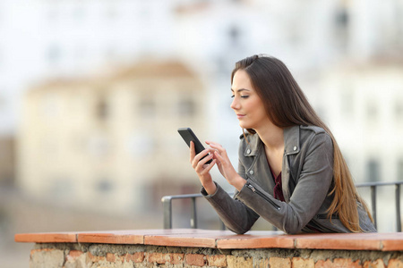 放松的女人在城里度假的阳台上用智能手机