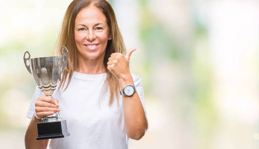 中年西班牙裔冠军妇女庆祝奖，在孤立的背景下捧着奖杯，开心地大笑着，做着好的，用手指签个名，好极了